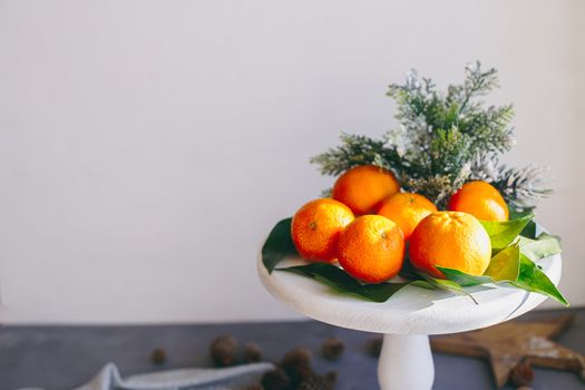 Orange tangerines on grey background in New Year's decor with brown pine cones and green leaves. Delicious sweet clementine. Christmas decoration with mandarins.