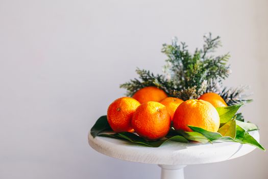 Orange tangerines on grey background in New Year's decor with brown pine cones and green leaves. Delicious sweet clementine. Christmas decoration with mandarins.