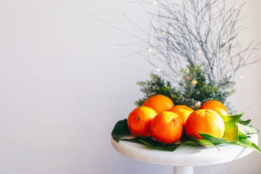 Orange tangerines on grey background in New Year's decor with brown pine cones and green leaves. Delicious sweet clementine. Christmas decoration with mandarins.