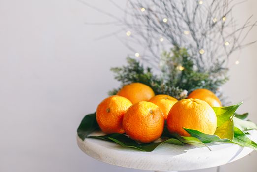 Orange tangerines on grey background in New Year's decor with brown pine cones and green leaves. Delicious sweet clementine. Christmas decoration with mandarins.