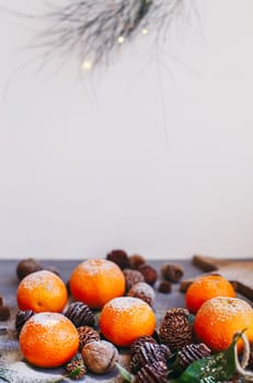 Orange tangerines on grey background in New Year's decor with brown pine cones and green leaves. Delicious sweet clementine. Christmas decoration with mandarins.