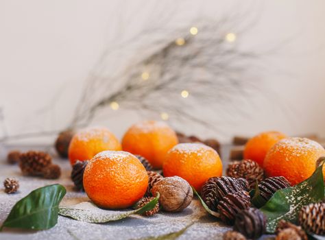 Orange tangerines on grey background in New Year's decor with brown pine cones and green leaves. Delicious sweet clementine. Christmas decoration with mandarins.