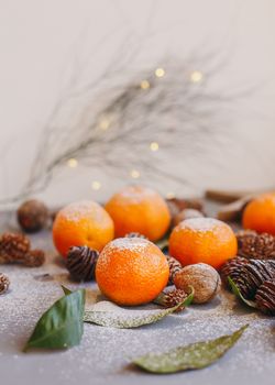 Orange tangerines on grey background in New Year's decor with brown pine cones and green leaves. Delicious sweet clementine. Christmas decoration with mandarins.