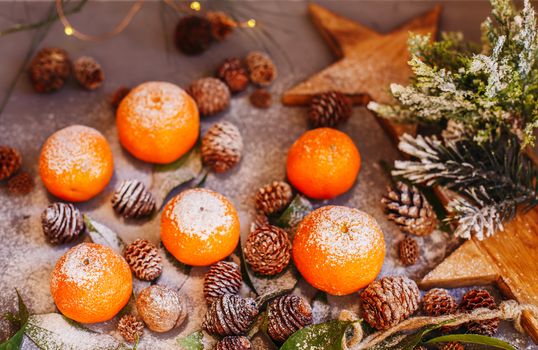 Orange tangerines on grey background in New Year's decor with brown pine cones and green leaves. Delicious sweet clementine. Christmas decoration with mandarins.