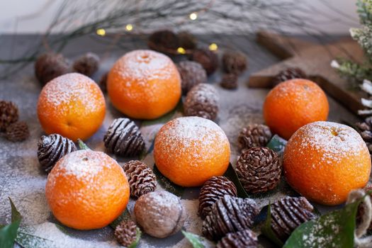 Orange tangerines on grey background in New Year's decor with brown pine cones and green leaves. Delicious sweet clementine. Christmas decoration with mandarins.