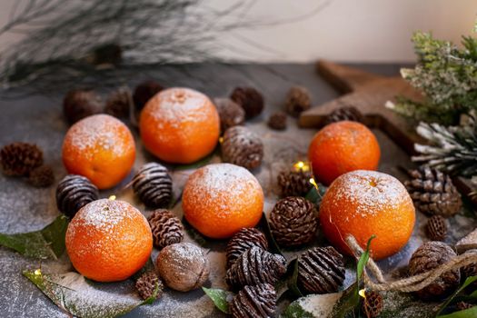 Orange tangerines on grey background in New Year's decor with brown pine cones and green leaves. Delicious sweet clementine. Christmas decoration with mandarins.