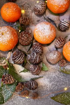 Orange tangerines on grey background in New Year's decor with brown pine cones and green leaves. Delicious sweet clementine. Christmas decoration with mandarins.