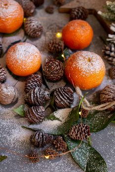 Orange tangerines on grey background in New Year's decor with brown pine cones and green leaves. Delicious sweet clementine. Christmas decoration with mandarins.