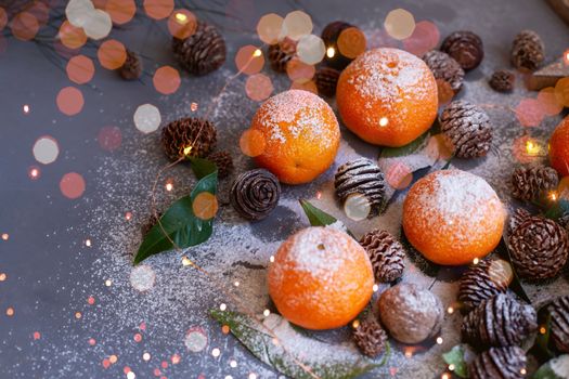 Orange tangerines on grey background in New Year's decor with brown pine cones and green leaves. Delicious sweet clementine. Christmas decoration with mandarins.