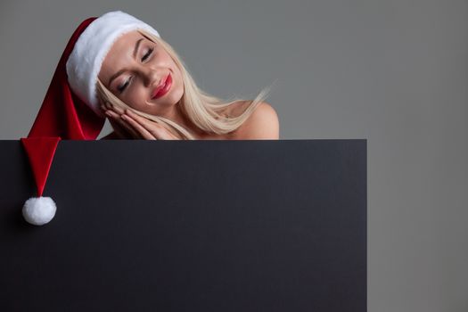 Santa girl holding blank black sign billboard. Christmas woman in Santa hat showing paper sign