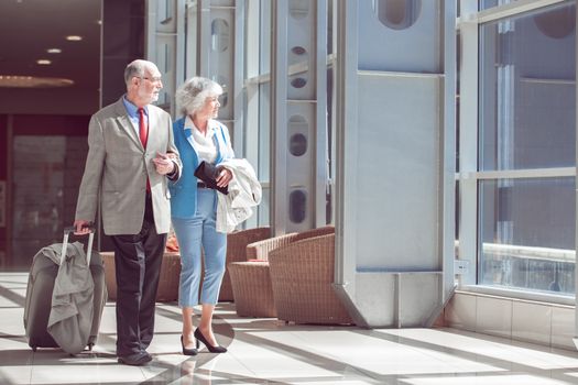 Happy elderly senior couple of travelers with suitcase in airport
