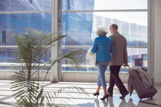 Happy elderly senior couple of travelers with suitcase in airport