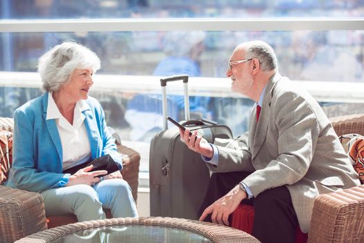 Happy elderly senior couple of travelers with suitcase in airport cafe waiting for flight