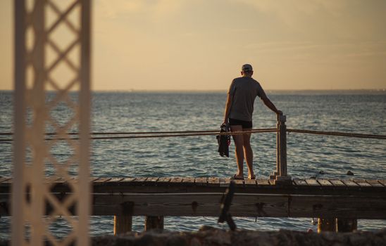 BAYAHIBE, DOMINICAN REPUBLIC 13 DECEMBER 2019: Man on the pier at sunset looks at the sea