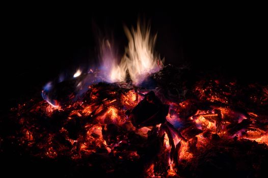 A low light long exposure photo of smouldering coals. Many coals and flames. Burning books and wood. 