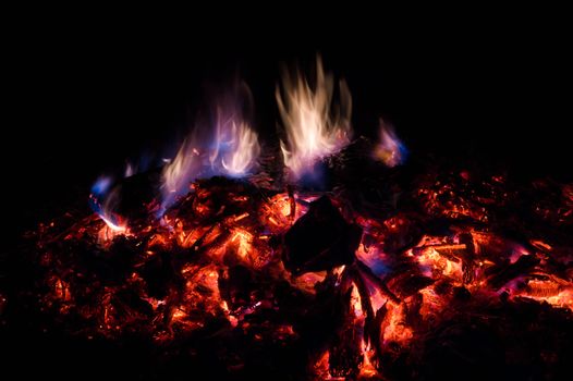 A low light long exposure photo of smouldering coals. Many coals and flames. Burning books and wood. 