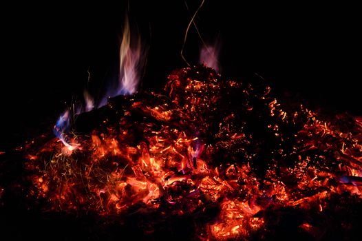 A low light long exposure photo of smouldering coals. Many coals and flames. Burning books and wood. 
