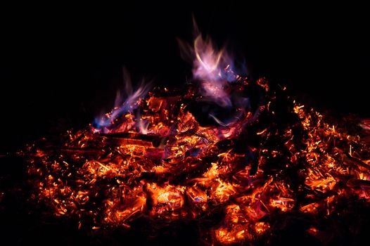 A low light long exposure photo of smouldering coals. Many coals and flames. Burning books and wood. 