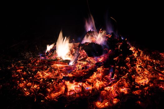 A low light long exposure photo of smouldering coals. Many coals and flames. Burning books and wood. 