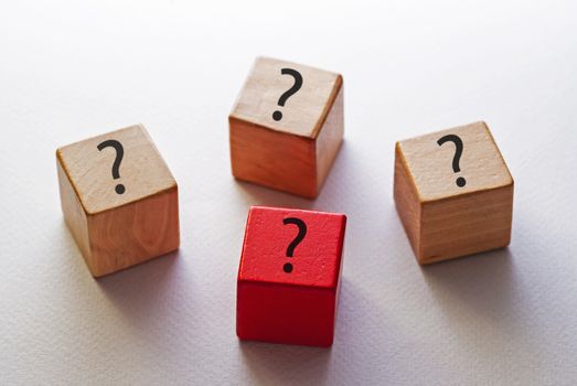 Concept of uniqueness and individuality with three identical wooden blocks with question marks and one red one on a white background viewed high angle