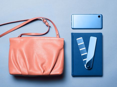 Pink coral female leather bag with accessories in classic blue 2020 color over blue background. Color of year 2020 concept for fashion and clothing industry.