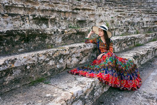 Woman in bohemian dress sitting on theater of Hierapolis ancient city in Pamukkale, Turkey.