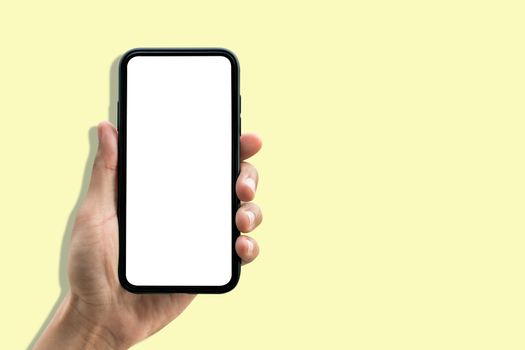 Hand holding smartphone on pastel yellow background.