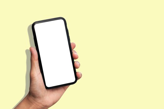 Hand holding smartphone on pastel yellow background.