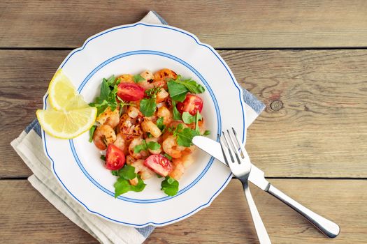 Fresh homemade salad of shrimp, arugula and tomato in a white plate on a wooden table, top view, flat lay.