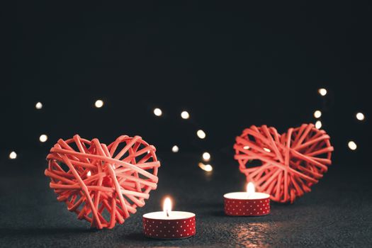 Romantic composition - two wicker hearts symbol of love, lights and a burning candles on a dark table. Valentines day concept.