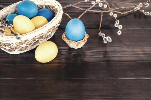 Easter composition - several colored eggs in a basket and on a dark wooden table with willow twigs, place for text, copy space.