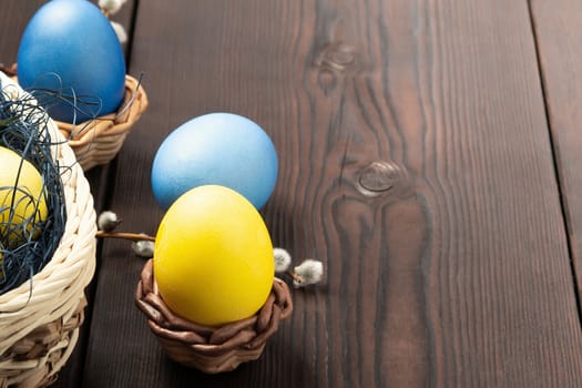 Easter composition - several colored eggs in a basket and on a dark wooden table with willow twigs, place for text, copy space.