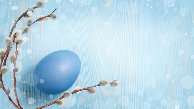 One blue egg on a blue wooden table with pussy-willow twigs - horizontal blank for design or greeting card, place for text, copy space.