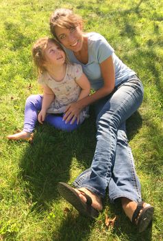 Young Mother and preschool child smilimg on grass in sunlight park