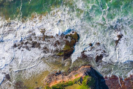 Tidal flows over coastal rocks and eroded chasms of a high tide. Aerial views background nature image. Motion in water