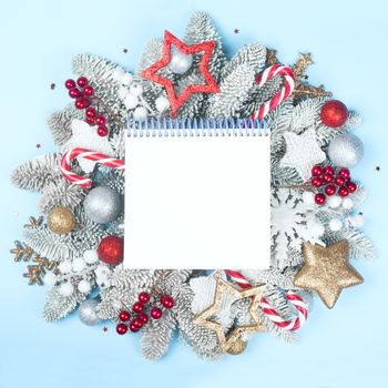 Frosted fir tree twigs and Christmas decorative bauble balls on blue background with white notebook with copy space for text template flat lay top view design
