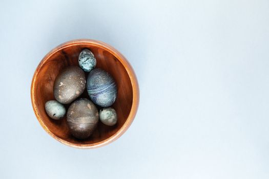 Creatively painted chicken and quail Easter eggs with natural hibiscus dye, look like sea stones in bowl on gray background, copy space. Happy Easter DIY concept. Soft slective focus. Flat lay.