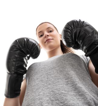 Bottom up portrait of a beautiful young woman with boxing gloves in a stance with raised arms looking down, isolated on white background.