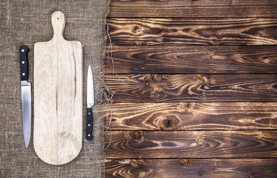 Old cutting board with knife on dark wooden table. Top view. Copy space