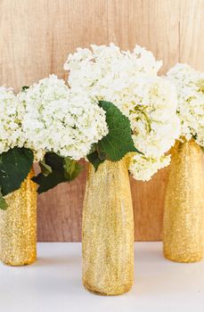 Golden glittered bottles with hydrangea flowers. White flowers in gold vases