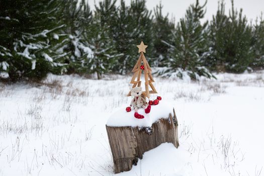 Christmas tree and Christmas ornaments on an old tree stump in snow covered landscape with snow falling.