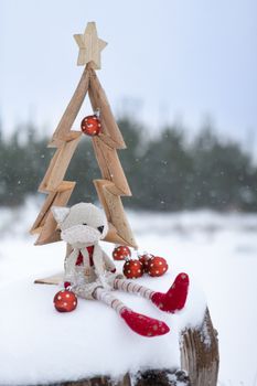 Simple rustic Christmas tree in the snow with Christmas baubles and Christmas decorations surrounding it as snow falls across the landscape