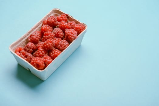 box of fresh raspberries on a blue background