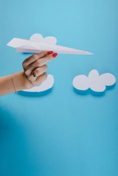 Paper plane in female hand on a blue background with clouds