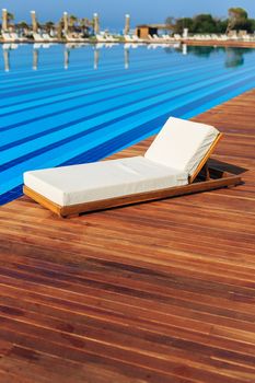 blue crystal clear water in the swimming pool with wooden beach lounger for the beach white color and wooden base