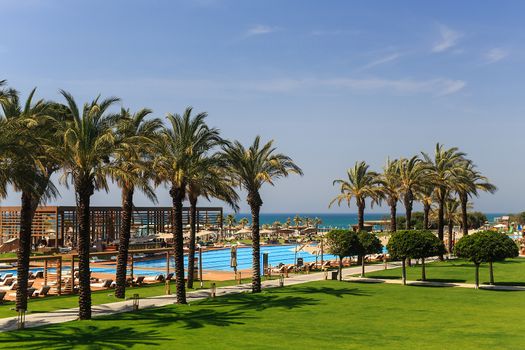 hotel grounds with swimming pool, clear blue sea and trees, summer Sunny day palm trees and sand