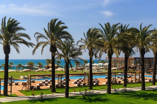 hotel grounds with swimming pool, clear blue sea and trees, summer Sunny day palm trees and sand