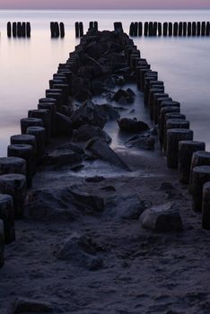 A photograph of wooden breakwater and seagulls at sunset on the Baltic Sea