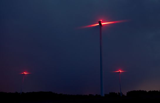 Wind turbines on a dramatic dark blue clouds in the sky. Storm ahead is coming. Red warning light on the windmill