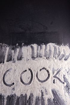 Word cook written with flour on black background.